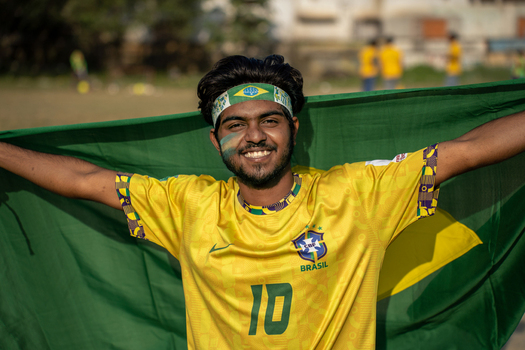 Bogura Bangladesh 18 November 2022 View of a young man wearing a Brazil football jersey and holding a large Brazilian flag with a smile.