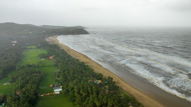 Aerial view of Gokarna beach with lush palm trees green fields and waves crashing on the sandy coastline in Gokarna Karnataka India.