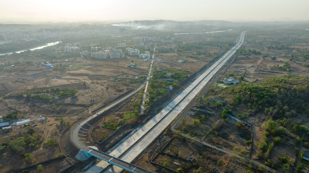 Aerial view of the JNPT Highway Badlapur Tunnel featuring a long concrete road stretching through the dry landscape with distant buildings under a hazy sky in Badlapur Maharashtra India. Aerial view of the JNPT Highway Badlapur Tunnel featuring a long concrete road stretching through the dry landscape with distant buildings under a hazy sky in Badlapur Maharashtra India.