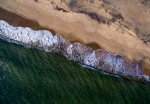 Aerial view of Katama Beach with waves crashing on the sandy shore and footprints visible on the sand in Edgartown Massachusetts United States. Aerial view of Katama Beach with waves crashing on the sandy shore and footprints visible on the sand in Edgartown Massachusetts United States.