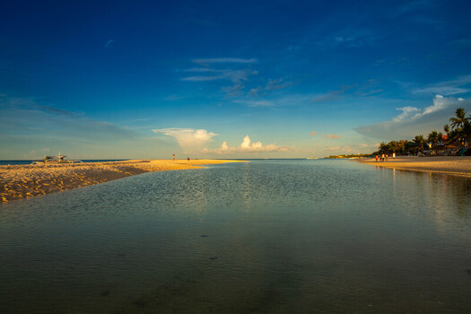 View of the sandy shores and calm waters of Bantayan Island with people walking along the beach under a clear blue sky in Cebu Central Visayas Philippines. View of the sandy shores and calm waters of Bantayan Island with people walking along the beach under a clear blue sky in Cebu Central Visayas Philippines.