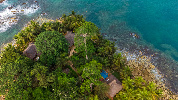 Axim Western Region Ghana 09 February 2023 Aerial view of Lou Moon Resort Eco Luxury with thatched roof villas nestled among palm trees and tropical vegetation along the rocky coastline. Axim Western Region Ghana 09 February 2023 Aerial view of Lou Moon Resort Eco Luxury with thatched roof villas nestled among palm trees and tropical vegetation along the rocky coastline.