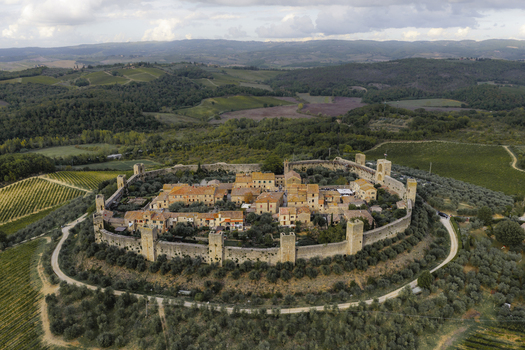 Aerial view of the medieval walled town of Monteriggioni featuring historic stone fortifications terracotta rooftops and surrounding olive groves and vineyards in Monteriggioni Tuscany Italy.