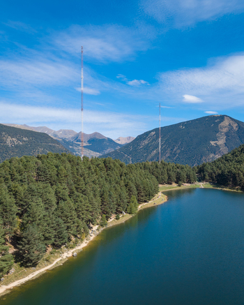 Aerial view of Lake Engolasters surrounded by dense pine forests and towering mountains under a clear blue sky Encamp Andorra. Aerial view of Lake Engolasters surrounded by dense pine forests and towering mountains under a clear blue sky Encamp Andorra.