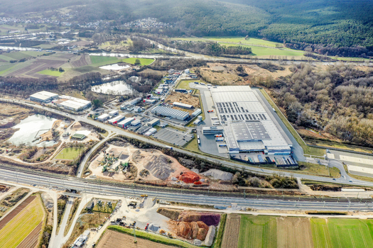 Aerial view of large industrial warehouses and commercial buildings surrounded by green fields and forested hills in Buttenheim Bavaria Germany. Aerial view of large industrial warehouses and commercial buildings surrounded by green fields and forested hills in Buttenheim Bavaria Germany.
