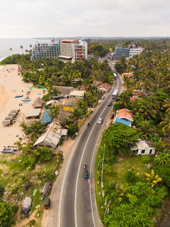 Aerial view of Dadalla beach and the coastal road lined with palm trees hotels and local houses under a cloudy sky in Galle Southern Province Sri Lanka. Aerial view of Dadalla beach and the coastal road lined with palm trees hotels and local houses under a cloudy sky in Galle Southern Province Sri Lanka.