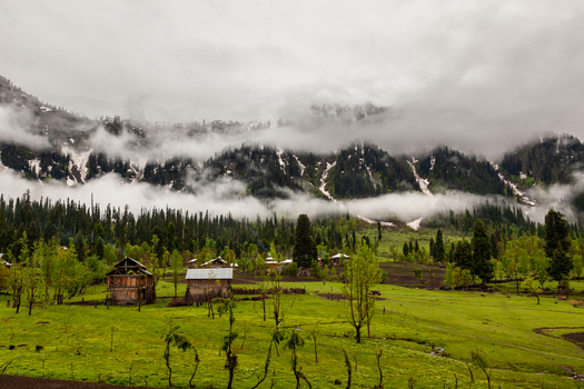 View of wooden houses on a lush green meadow in Neelum Valley surrounded by pine forests and misty mountains Arang Kel Azad Kashmir Pakistan. View of wooden houses on a lush green meadow in Neelum Valley surrounded by pine forests and misty mountains Arang Kel Azad Kashmir Pakistan.