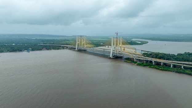 Aerial view of the Zuari Bridge spanning the river with lush green banks and cloudy skies in Cortalim Goa India.