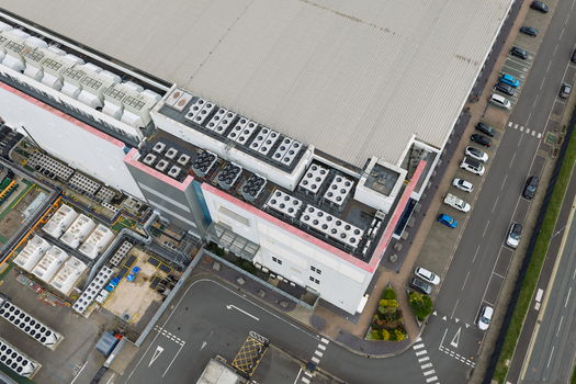 Aerial view of a large data center facility featuring numerous rooftop cooling units adjacent parking area with parked vehicles and industrial infrastructure in the United Kingdom.