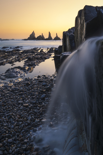 View of the sharp sea stacks of Gueirua beach with long exposure silky water flowing over dark rocks during a golden sunset in Asturias Asturias Spain.