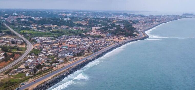 Aerial view of a coastal town with residential buildings and a road running along the shoreline of the Atlantic Ocean in Ghana. Aerial view of a coastal town with residential buildings and a road running along the shoreline of the Atlantic Ocean in Ghana.