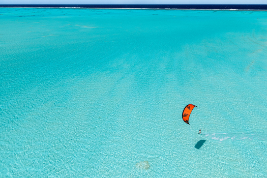 Aerial view of a kitesurfer with an orange kite gliding over the clear turquoise waters of the Aitutaki lagoon Aitutaki Cook Islands. Aerial view of a kitesurfer with an orange kite gliding over the clear turquoise waters of the Aitutaki lagoon Aitutaki Cook Islands.