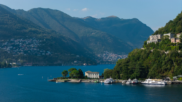 Aerial view of Lake Como with a historic villa on the shore boats docked at the pier surrounded by lush green mountains and clear blue water in Como Lombardy Italy.