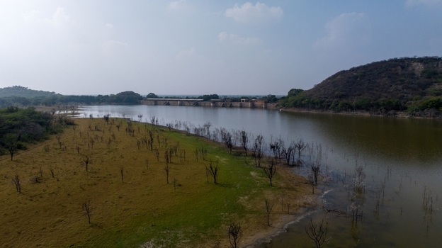 Aerial view of a serene lake surrounded by dry landscape sparse trees and distant hills under a clear blue sky in Jodhpur Rajasthan India. Aerial view of a serene lake surrounded by dry landscape sparse trees and distant hills under a clear blue sky in Jodhpur Rajasthan India.