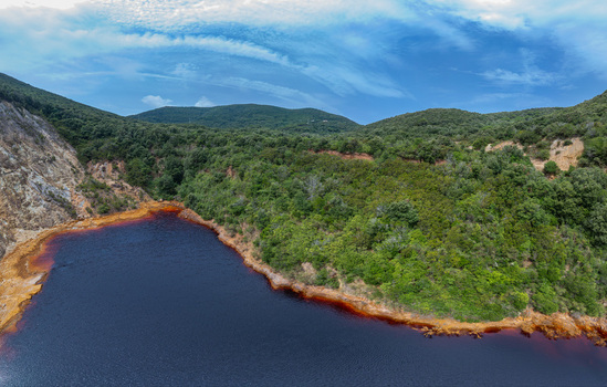 Aerial view of the red colored Laghetto delle conche surrounded by lush green hills and dense forest in Rio Marina Toscana Italy.