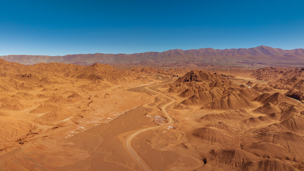 Aerial view of the arid desert landscape with winding dirt roads and rugged red rock formations in Tolar Grande Salta Province Argentina. Aerial view of the arid desert landscape with winding dirt roads and rugged red rock formations in Tolar Grande Salta Province Argentina.