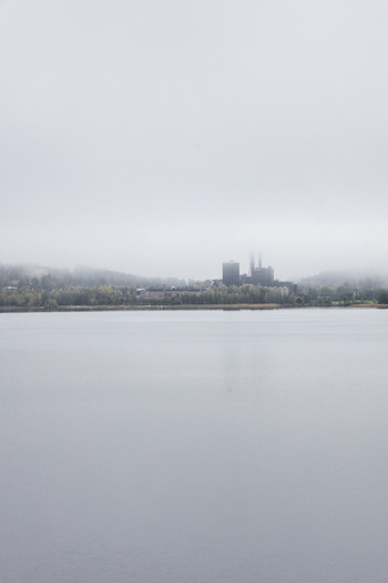 View of an industrial facility across a calm lake surrounded by trees under a thick layer of fog in Jyvaskyla Central Finland Finland.