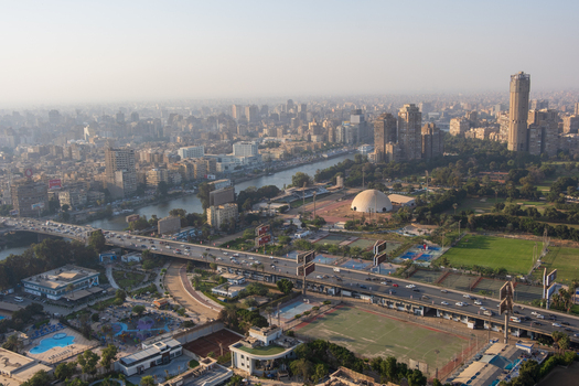 View of the bustling city unfolds with a river winding through buildings bridges and lush green spaces under a hazy sky Zamalek Cairo Governorate Egypt. View of the bustling city unfolds with a river winding through buildings bridges and lush green spaces under a hazy sky Zamalek Cairo Governorate Egypt.