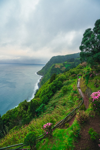 Aerial view of a vibrant coastline where emerald hills plunge into the deep blue Atlantic framed by a cloudy sky Nordeste Azores Portugal.