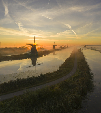 Aerial view of historic windmills at Unesco World Heritage Kinderdijk reflected in the misty canal during a golden sunrise Kinderdijk Zuid Holland Netherlands.