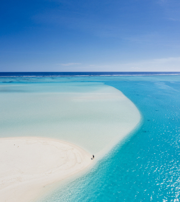 Aerial view of a lone person standing on a white sandbar surrounded by vibrant turquoise lagoon waters in Aitutaki Cook Islands. Aerial view of a lone person standing on a white sandbar surrounded by vibrant turquoise lagoon waters in Aitutaki Cook Islands.
