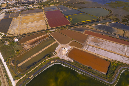 Aerial view of Salinas do Grelha salt pans featuring vibrant red brown and green water basins separated by dirt paths in Olhao Faro Portugal. Aerial view of Salinas do Grelha salt pans featuring vibrant red brown and green water basins separated by dirt paths in Olhao Faro Portugal.
