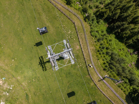 Aerial view of a cable car pylon and a moving cabin over a lush green alpine meadow in the mountains near Imst Tyrol Austria.