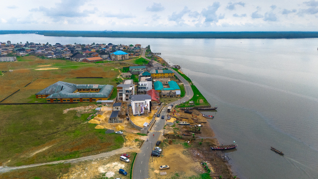 Aerial view of a coastal settlement with residential buildings a winding road and wooden boats moored along the riverbank in Minima Rivers Nigeria.