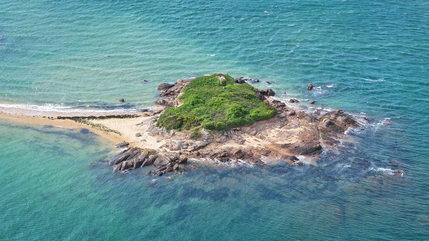 Aerial view of a small rocky island with lush green vegetation surrounded by turquoise sea water and ripples Carantec Brittany France. Aerial view of a small rocky island with lush green vegetation surrounded by turquoise sea water and ripples Carantec Brittany France.