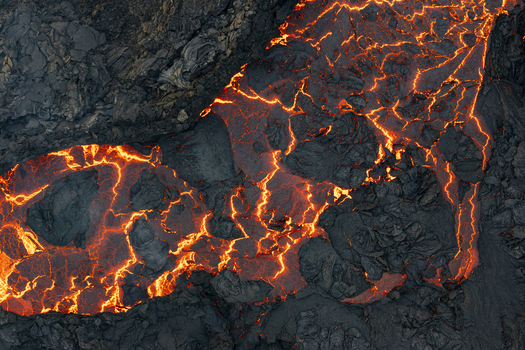 Aerial view of fiery molten lava snaking through the dark jagged volcanic landscape a stark contrast of destruction and raw beauty Reykjavik Reykjanes Iceland.
