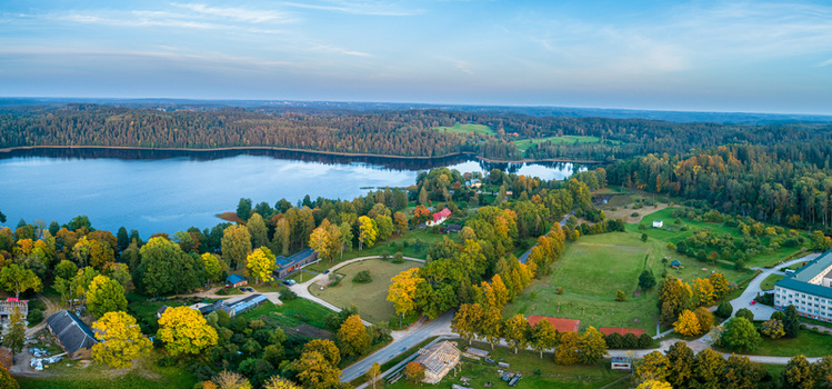 Aerial view of a serene lake surrounded by dense autumn forests scattered rural buildings and open fields in Latvia. Aerial view of a serene lake surrounded by dense autumn forests scattered rural buildings and open fields in Latvia.