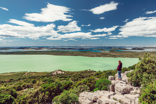 View of a woman standing on a rocky cliff overlooking the green waters of Lake Vrana with the Adriatic Sea in the distance Vrana Zadar County Croatia. View of a woman standing on a rocky cliff overlooking the green waters of Lake Vrana with the Adriatic Sea in the distance Vrana Zadar County Croatia.