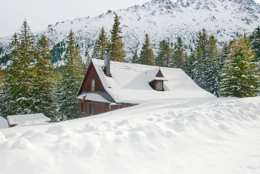 View of a traditional wooden mountain hut covered in thick snow surrounded by evergreen trees and rugged peaks Tatra County Lesser Poland Voivode Poland. View of a traditional wooden mountain hut covered in thick snow surrounded by evergreen trees and rugged peaks Tatra County Lesser Poland Voivode Poland.