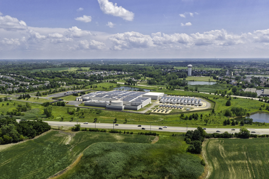 Aerial view of a modern data center facility with solar panels on the roof and cooling units surrounded by green fields and a road in Volo Illinois United States. Aerial view of a modern data center facility with solar panels on the roof and cooling units surrounded by green fields and a road in Volo Illinois United States.