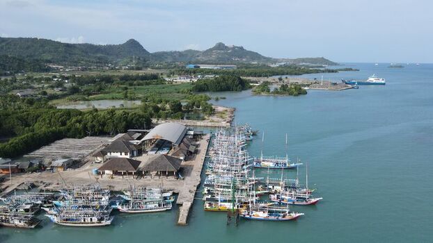Bakauheni Indonesia 15 December 2021 Aerial view of the Bakauheni harbor with numerous fishing boats docked at the pier surrounded by lush coastal vegetation and rolling hills.