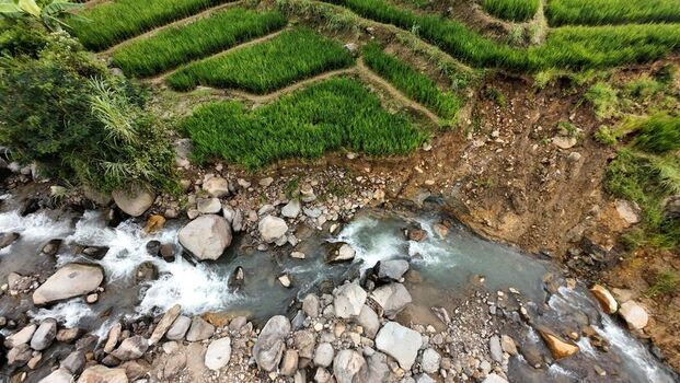 Aerial view of green terraced rice fields and a rocky river with a visible landslide area in Sukamakmur West Java Indonesia. Aerial view of green terraced rice fields and a rocky river with a visible landslide area in Sukamakmur West Java Indonesia.