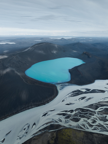 Aerial view of a turquoise glacial lake nestled within black volcanic mountains juxtaposed against the stark white glacier river creating a scene of ethereal beauty Highlands Iceland.