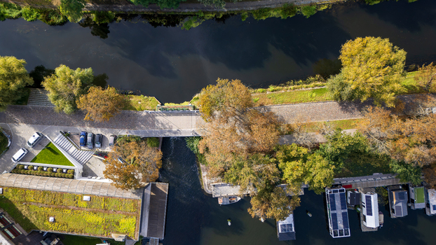 Aerial view of the vibrant Brda River flowing under a quaint bridge flanked by autumnal trees and houseboats Bydgoszcz Województwo kujawsko pomorskie Poland. Aerial view of the vibrant Brda River flowing under a quaint bridge flanked by autumnal trees and houseboats Bydgoszcz Województwo kujawsko pomorskie Poland.