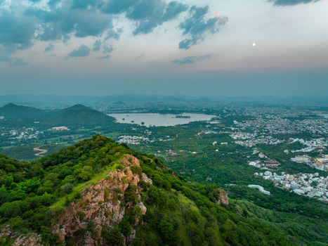 Aerial view of the lush green hills and Lake Pichola surrounding the city of Udaipur at twilight with a crescent moon in the sky Udaipur Rajasthan India.