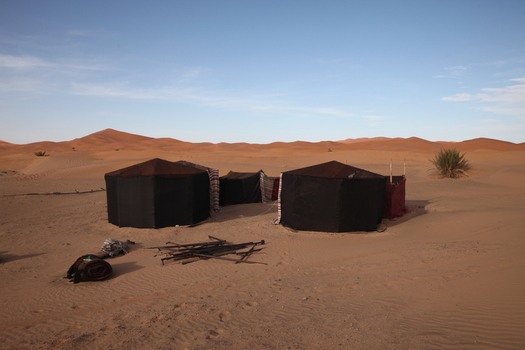 View of traditional black nomadic tents set in the vast Sahara desert landscape under a clear blue sky in Morocco.
