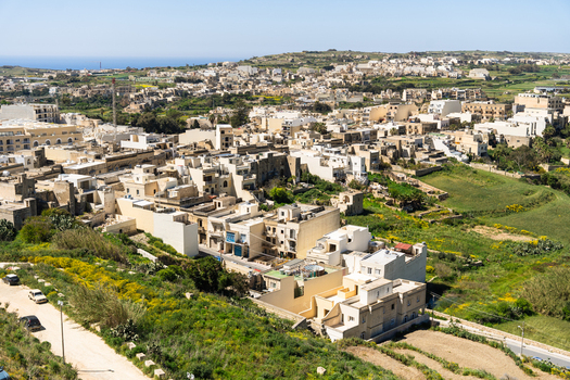View of traditional limestone houses and narrow streets surrounded by lush green hills and fields under a clear blue sky in Zebbug Gozo Region Malta. View of traditional limestone houses and narrow streets surrounded by lush green hills and fields under a clear blue sky in Zebbug Gozo Region Malta.