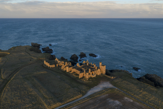 Aerial view of the historic Slains Castle ruins on the edge of steep cliffs overlooking the North Sea at golden hour in Cruden Bay Scotland United Kingdom. Aerial view of the historic Slains Castle ruins on the edge of steep cliffs overlooking the North Sea at golden hour in Cruden Bay Scotland United Kingdom.