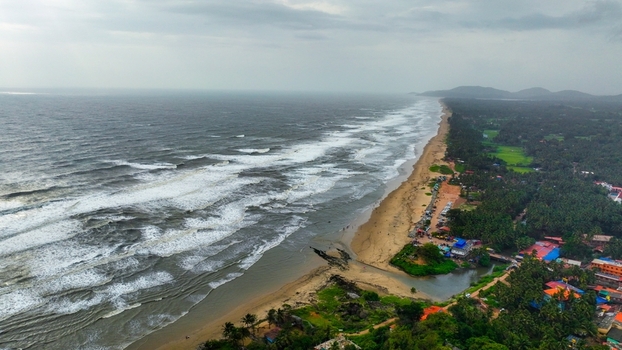 Aerial view of Gokarna Main Beach featuring the expansive coastline crashing waves lush palm trees and coastal buildings in Gokarna Karnataka India.