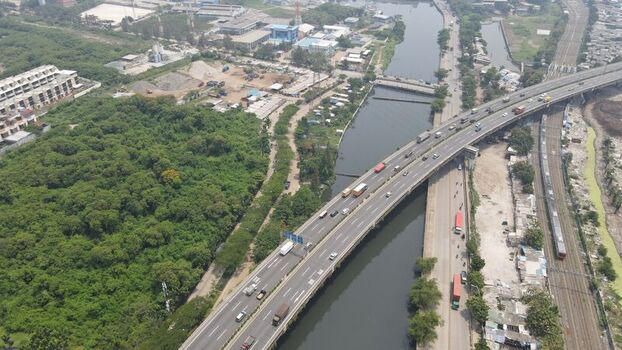Aerial view of a busy highway bridge crossing a river with surrounding green vegetation industrial buildings and a railway line in Tanjung Priok Jakarta Indonesia. Aerial view of a busy highway bridge crossing a river with surrounding green vegetation industrial buildings and a railway line in Tanjung Priok Jakarta Indonesia.