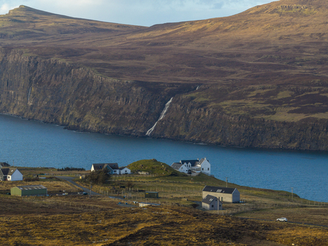Aerial view of the coastal village of Milovaig featuring white houses and a waterfall cascading down steep cliffs into the sea Milovaig Scotland United Kingdom.