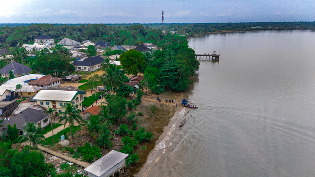 Aerial view of a riverside village with houses lush trees a small wooden pier and boats on the water in Minima Rivers Nigeria.