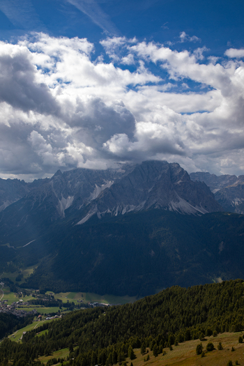 Aerial view of the Dolomites mountain range with dramatic clouds rugged rocky peaks and lush green forests in the valley near Rocca Pietore Veneto Italy.