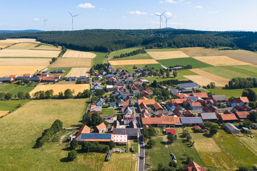 Aerial view of the rural village surrounded by agricultural fields meadows and wind turbines in the background near Burghaun Hessen Germany. Aerial view of the rural village surrounded by agricultural fields meadows and wind turbines in the background near Burghaun Hessen Germany.