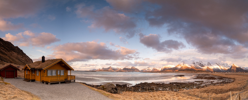 Nordland Norway 21 September 2026 Aerial view of a yellow cabin with a grass roof in Lofoten with snow capped mountains and a calm bay under a soft sunset sky. Nordland Norway 21 September 2026 Aerial view of a yellow cabin with a grass roof in Lofoten with snow capped mountains and a calm bay under a soft sunset sky.