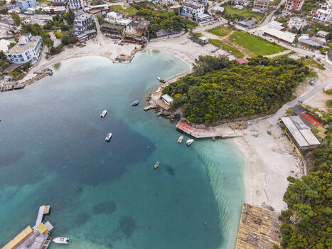 Aerial view of the coastal landscape featuring turquoise waters small boats moored in the bay sandy beaches and lush green vegetation in Ksamil Vlore County Albania. Aerial view of the coastal landscape featuring turquoise waters small boats moored in the bay sandy beaches and lush green vegetation in Ksamil Vlore County Albania.